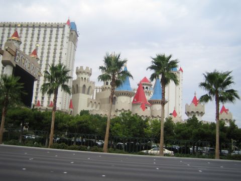1985 Ford Mustang - A view of the Excalibur Hotel and Casino on a cloudy day, with palm trees lining the street.