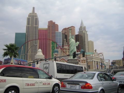 1985 Ford Mustang - Traffic moves past the New York-New York Hotel and Casino in Las Vegas, with iconic skyscrapers and the Statue of Liberty replica visible.