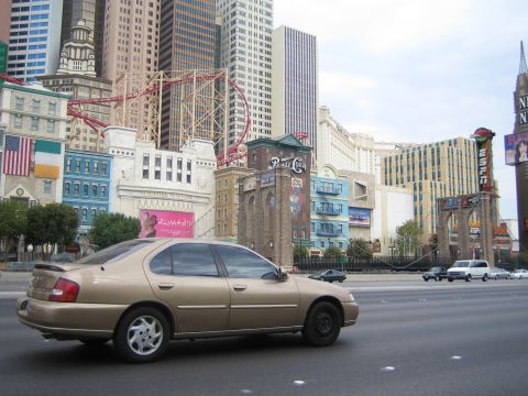 1985 Ford Mustang - A tan sedan is seen driving on a highway with the distinctive architecture of the New York-New York Hotel & Casino in Las Vegas in the back…