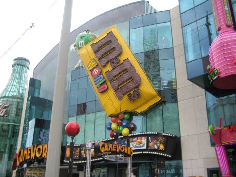 1985 Ford Mustang - Exterior view of the M&M's World store, a large M&M candy bar sign and colorful M&M characters.
