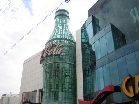 1985 Ford Mustang - A large, green glass Coca-Cola bottle structure is part of a building's facade, the iconic 'Cola' logo.