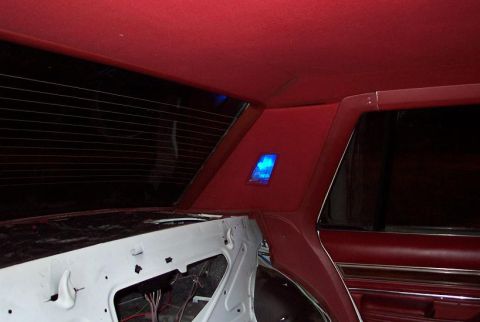 1985 Ford LTD Crown Victoria - Interior shot looking up at the red headliner and C-pillar of a sedan, with a blue-lit courtesy lamp glowing in the rear quarter trim panel…
