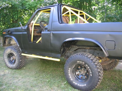 1986 Ford Bronco - This black SUV features a prominent yellow roll cage and aggressive off-road tires, viewed from the side.