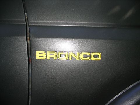 1986 Ford Bronco - Close-up of a yellow Bronco emblem affixed to the side of a vehicle.