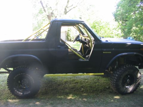 1986 Ford Bronco - This modified Ford Bronco features a prominent yellow roll cage and side steps, with its doors removed.