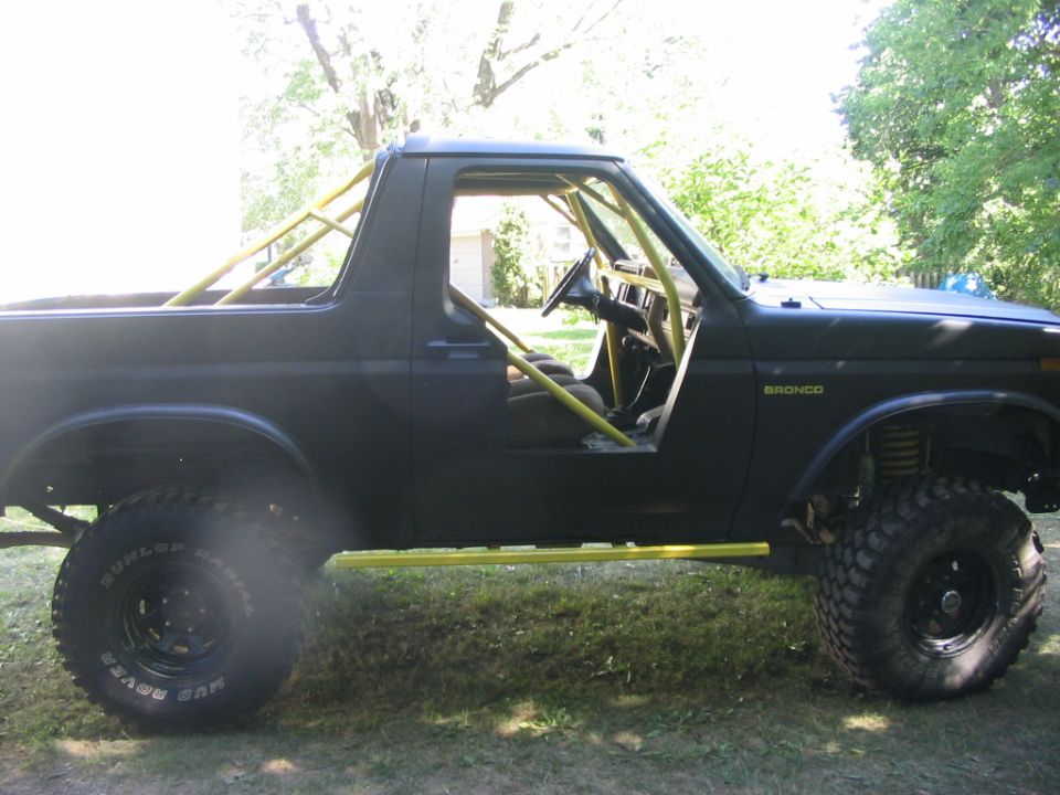 Black Ford Bronco with yellow roll cage and side steps, seen from the side