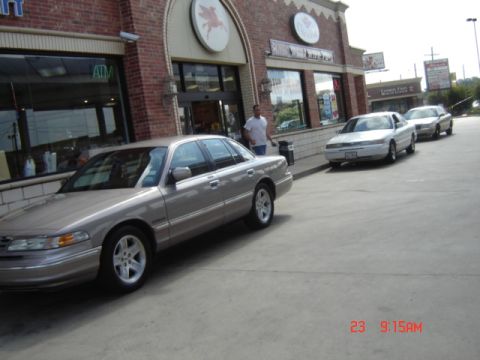 1988 Ford LTD Crown Victoria - Three sedans are parked outside a brick building with large windows and an ATM.