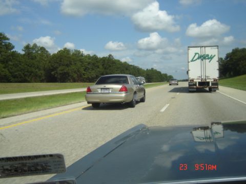 1988 Ford LTD Crown Victoria - A gold sedan travels down the highway, passing a large semi-truck under a cloudy sky.