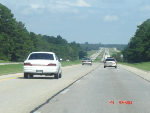 1988 Ford LTD Crown Victoria - Cars travel down a long, straight highway under a partly cloudy sky.