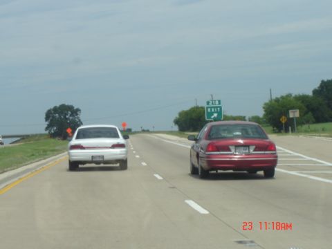 1988 Ford LTD Crown Victoria - Two sedans travel down the highway, with an exit sign for 218 in the distance.