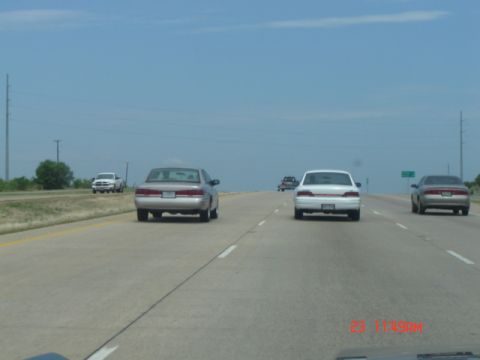 1988 Ford LTD Crown Victoria - Several cars drive down a highway under a clear blue sky.