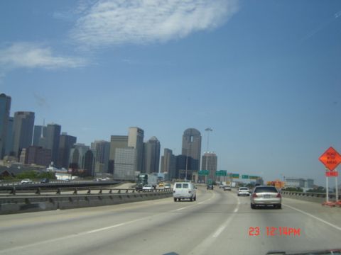 1988 Ford LTD Crown Victoria - Cars drive on a highway with the Dallas skyline visible under a partly cloudy sky.