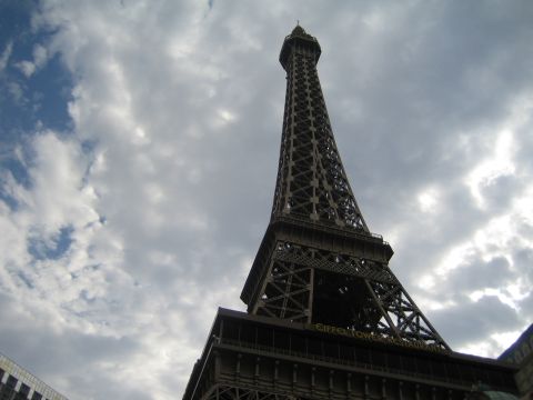 1985 Ford Mustang - A replica of the Eiffel Tower stands tall against a dramatic sky, with a restaurant sign visible at its base.