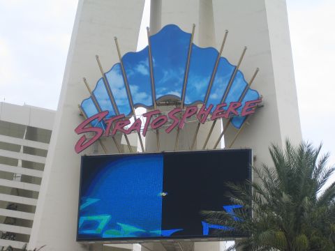 1985 Ford Mustang - The iconic Stratosphere hotel sign is visible against a cloudy sky, with a digital billboard displaying abstract blue graphics.