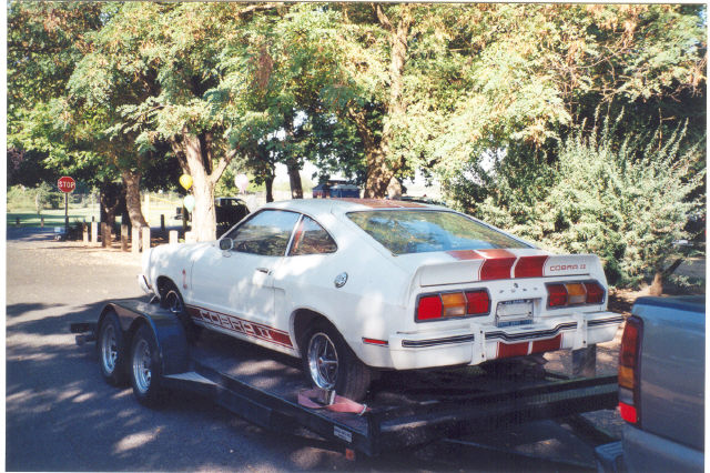 White 1978 Ford Mustang II Cobra II on a trailer, rear view, red stripes on hood and trunk, red stripe along the side