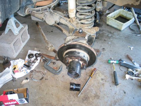 1995 Ford Bronco - Front hub and brake rotor removed from a 4x4 and laid on a concrete garage floor, with the truck's coil spring, radius arm and axle beam ab…