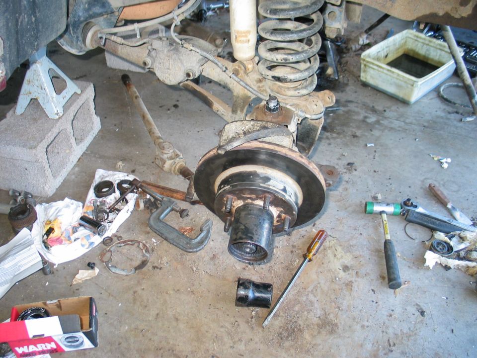 Front hub and brake rotor removed from a 4x4 axle on a garage floor with tools