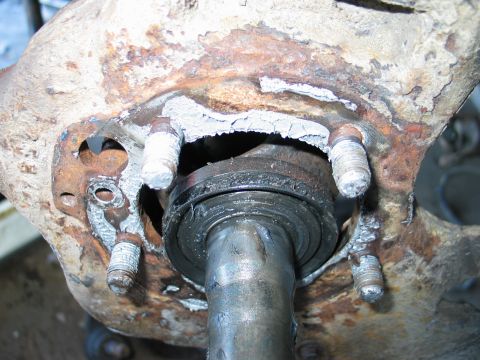 1995 Ford Bronco - Close-up of a heavily rusted steering knuckle with the hub removed, exposing the axle shaft, inner seal and four threaded wheel studs. Flak…