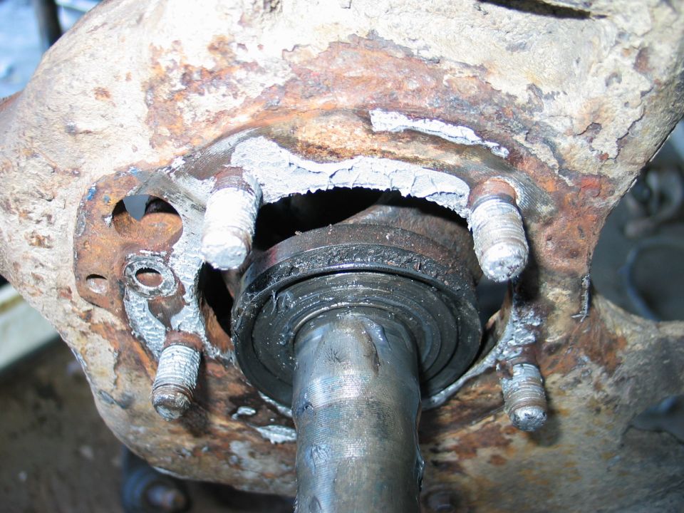 Rusty steering knuckle with hub removed exposing axle shaft, seal and wheel studs
