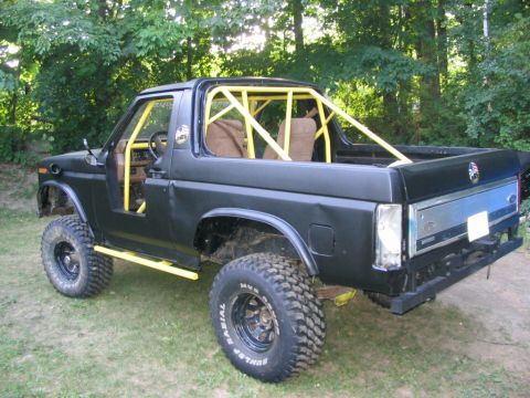 1986 Ford Bronco - This modified SUV features a prominent yellow roll cage and lifted suspension, with the front fender removed.