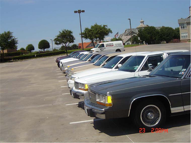 Dark gray sedan parked in a lot, showing its front quarter panel and wheel. The car has chrome trim and a rectangular headlight