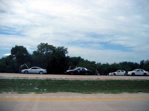 2000 Ford Crown Victoria - Several police cars and a civilian vehicle are stopped on the side of a road under a cloudy sky.