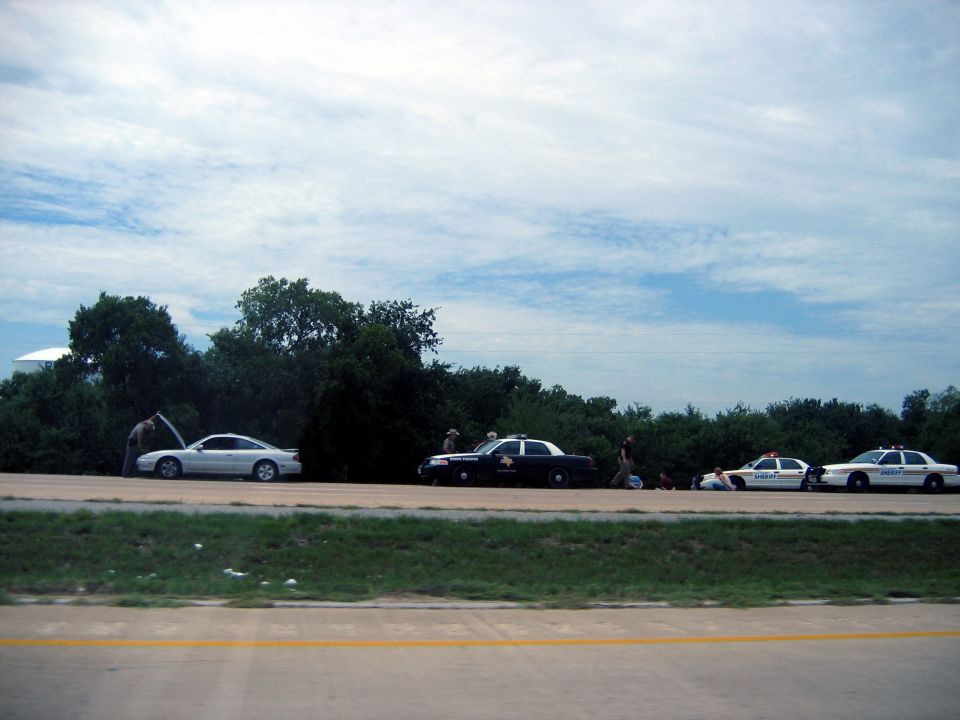 Silver sedan with hood open, flanked by three police cars on a roadside