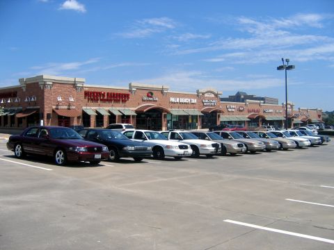 2000 Ford Crown Victoria - Row of full-size Ford and Mercury sedans parked in a strip-mall lot, led by a maroon Mercury Marauder on chrome wheels and followed by blac…