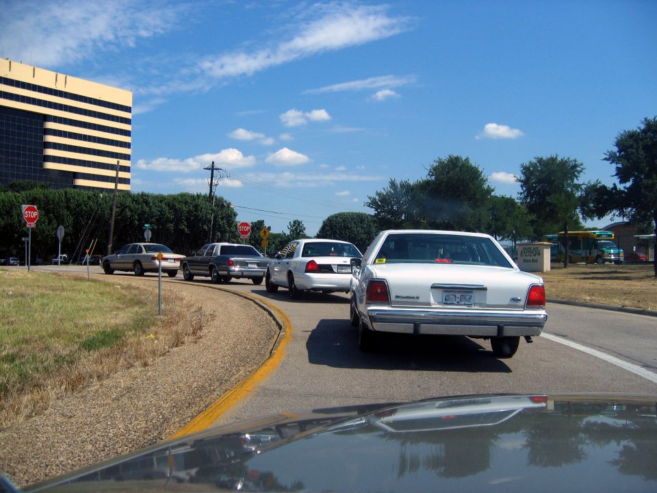 Four cars in a line on a road, one white Ford Crown Victoria in the foreground