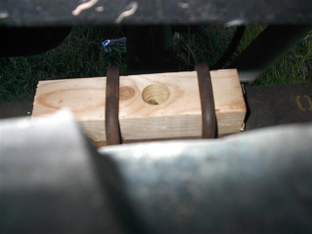 Wooden block held by metal straps under a vehicle part