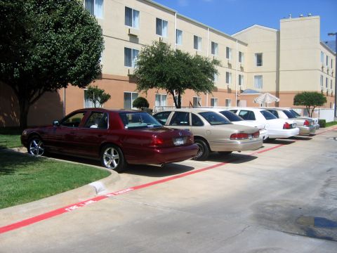 2000 Ford Crown Victoria - Several sedans, including a maroon 2000 Ford Crown Victoria, are parked in a lot outside a building.