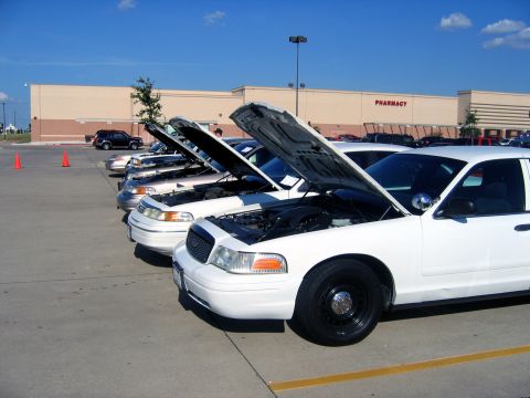 2000 Ford Crown Victoria - A row of white Ford Crown Victoria police cars are parked with their hoods open under a clear blue sky.