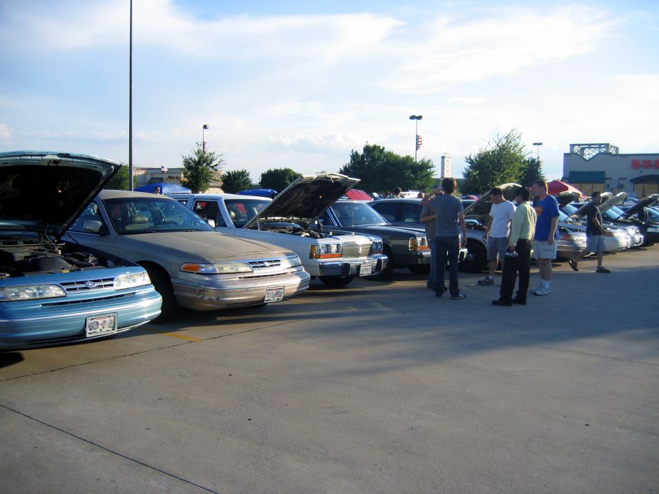 Several Ford Crown Victorias parked in a lot, hoods up. One is light blue, another is silver