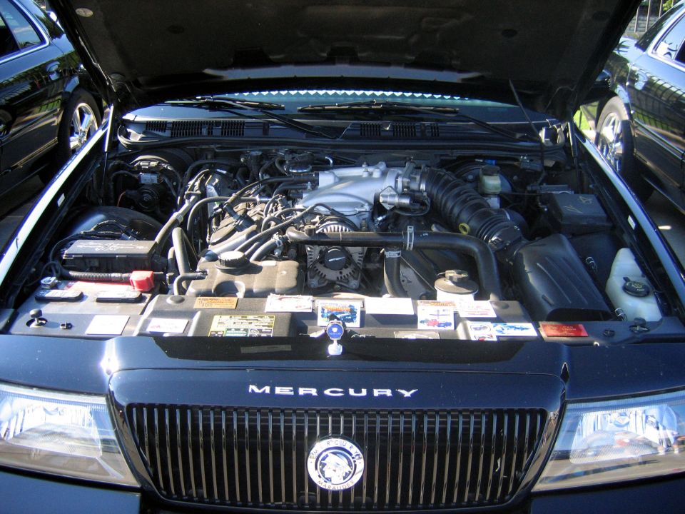 Engine bay of a Mercury with chrome grille and MERCURY lettering, hood up