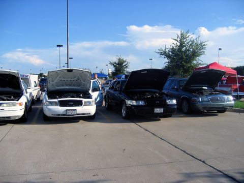 2000 Ford Crown Victoria - Cars are lined up with their hoods open at an outdoor event under a blue sky with clouds.