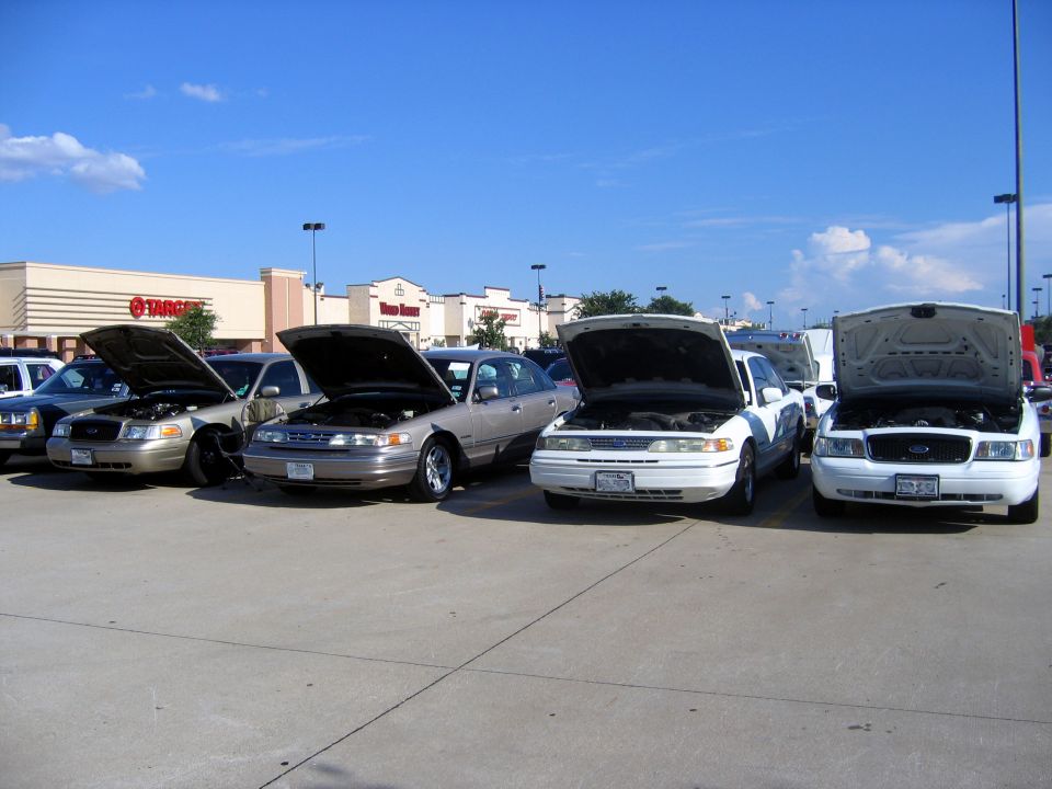 Four Ford Crown Victorias parked in a lot, hoods up. Two are tan, two are white. A Target store is in the background