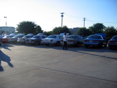2000 Ford Crown Victoria - Several Ford Crown Victorias are parked in a lot, with some owners attending to their vehicles.