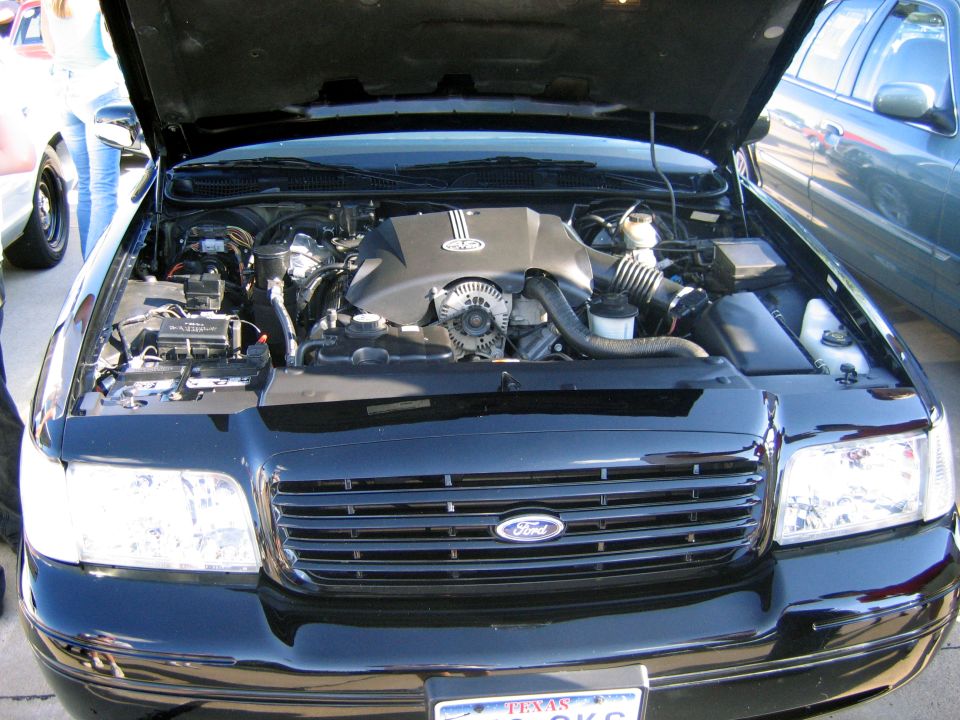Black Ford with hood up showing V8 and chrome grille at a car show