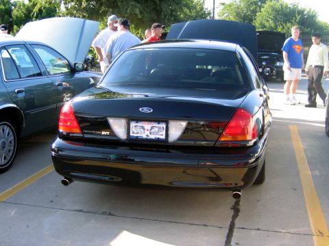 2000 Ford Crown Victoria - A group of people stand around cars with hoods up at an outdoor gathering.