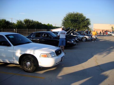 2000 Ford Crown Victoria - A white 2000 Ford Crown Victoria is parked in the foreground at a car meet, with other vehicles visible in the background.
