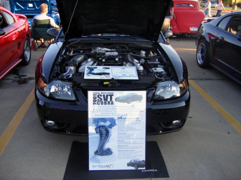 2000 Ford Crown Victoria - 2001 Ford Mustang SVT Cobra on display with hood open and information sign.