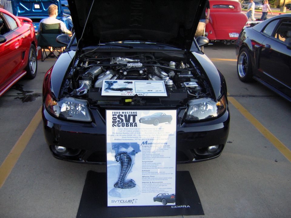Black 2001 Ford Mustang SVT Cobra with hood open, display sign in front. Red car and black car visible