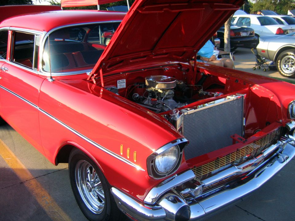 Red 1957 Chevrolet Bel Air with hood open, showing engine. Other cars in background