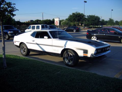 2000 Ford Crown Victoria - A white 1971 Ford Mustang Mach 1 is parked in a lot with other vehicles visible in the background.