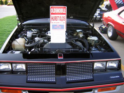2000 Ford Crown Victoria - This Oldsmobile Hurst Olds is displayed with its hood open, revealing the engine compartment and a prominent sign.