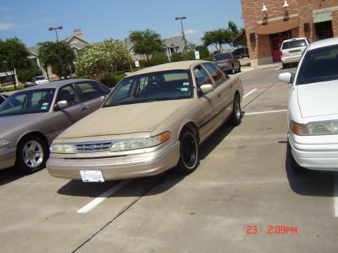 1988 Ford LTD Crown Victoria - Two Ford Crown Victorias parked in a lot, one tan and one white.