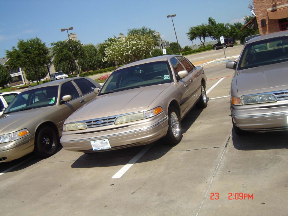 Tan 1990s Ford Crown Victoria sedan parked in a lot, front 3/4 view