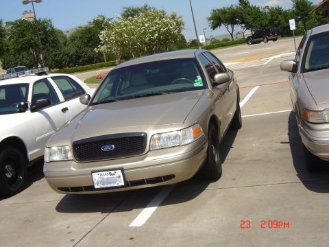 1988 Ford LTD Crown Victoria - A gold Ford Crown Victoria is parked in a lot next to a white police car.