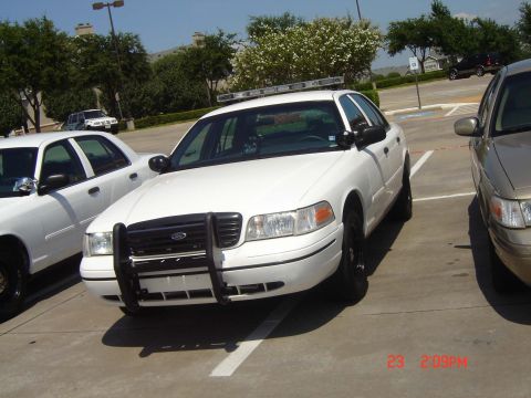 1988 Ford LTD Crown Victoria - A white police car is parked in a lot next to another vehicle.