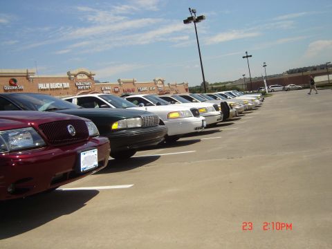 1988 Ford LTD Crown Victoria - A row of vehicles, including what appear to be police cruisers, are parked in a lot on a sunny day.